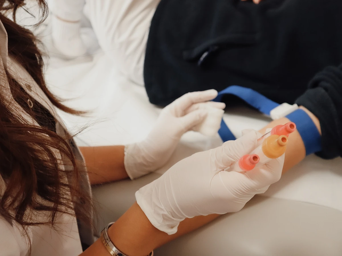 Blutabnahme im Cell Spa: behandschuhte Hände mit Blutröhrchen am Arm der Patientin