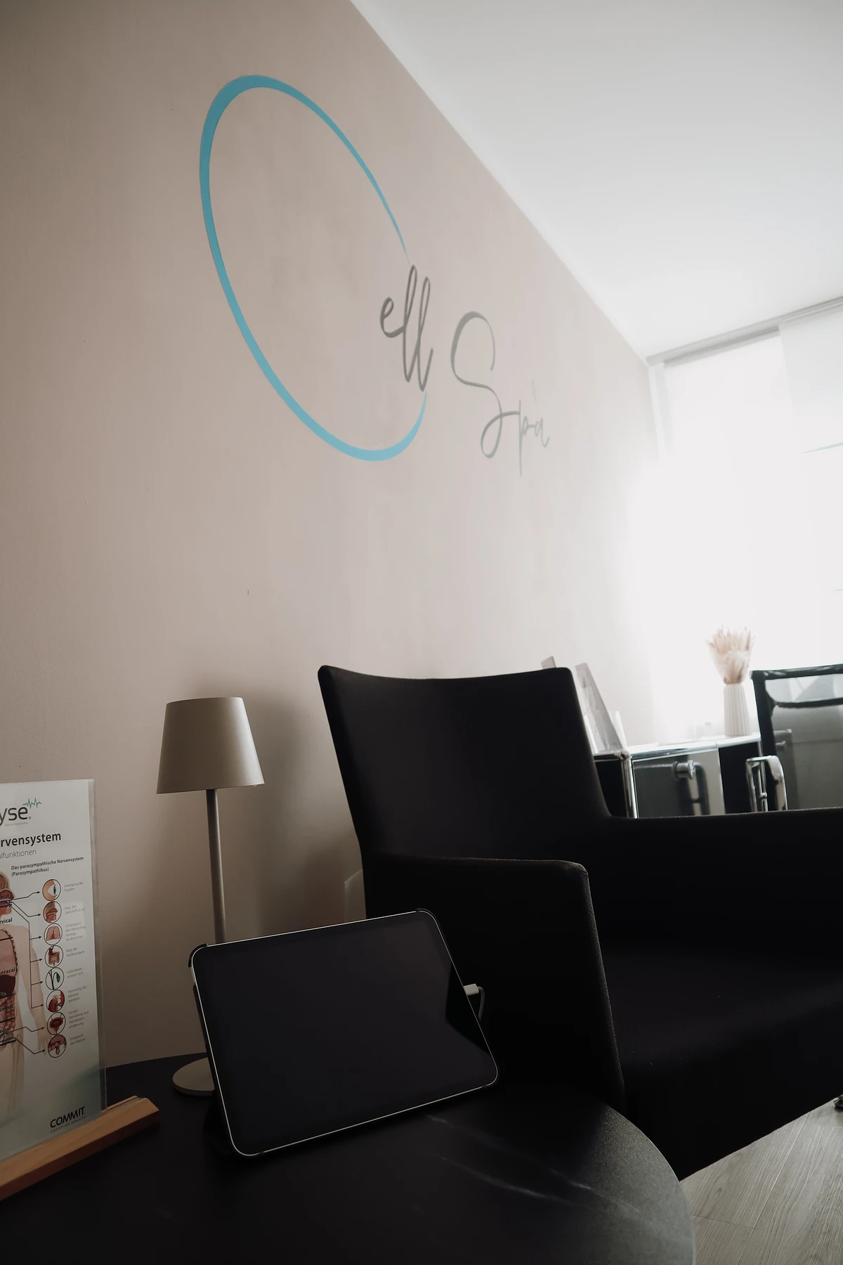 Behandlungsraum des Cell Spa mit Sessel, Stehlampe und dem Cell-Spa-Logo an der Wand